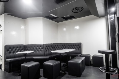 Salle voûtée en pierre avec éclairage LED coloré, mobilier minimaliste et comptoir de bar au fond.