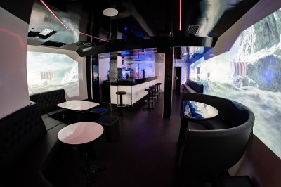Salle voûtée en pierre avec éclairage LED coloré, mobilier minimaliste et comptoir de bar au fond.