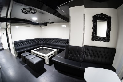 Salle voûtée en pierre avec éclairage LED coloré, mobilier minimaliste et comptoir de bar au fond.