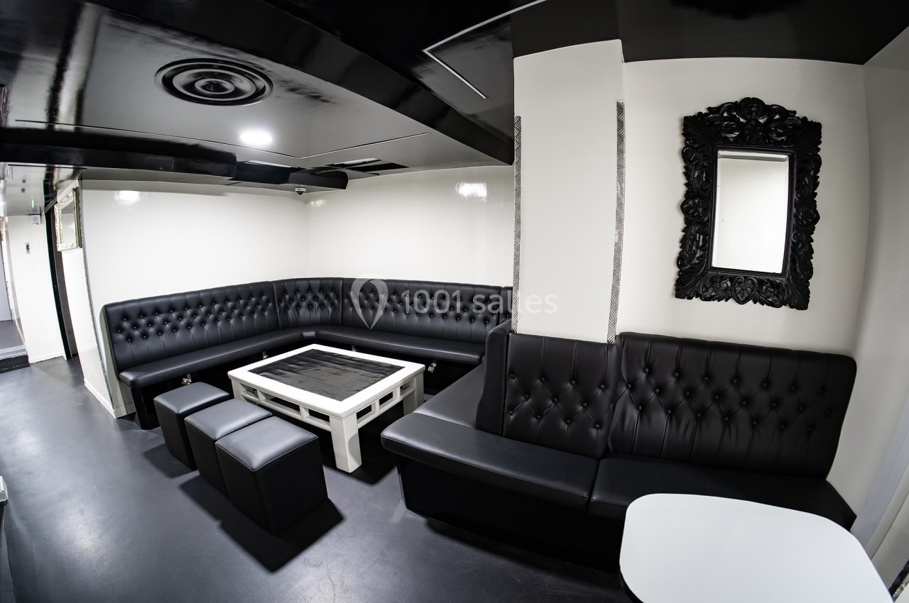 Salon moderne avec banquettes en cuir noir, table basse blanche, miroir encadré et éclairage minimaliste.