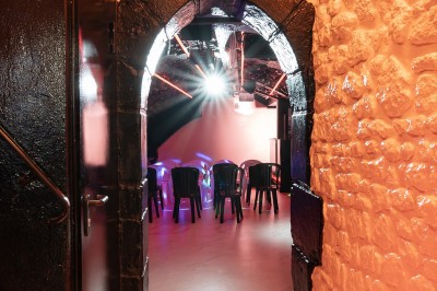 Salle voûtée en pierre avec éclairage LED coloré, mobilier minimaliste et comptoir de bar au fond.