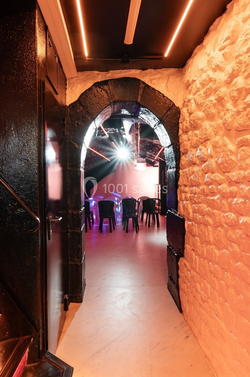 Vue d'une salle voûtée en pierre avec des chaises noires disposées sous un éclairage coloré.