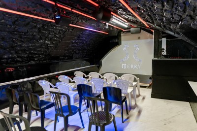 Salle voûtée en pierre avec éclairage LED coloré, mobilier minimaliste et comptoir de bar au fond.