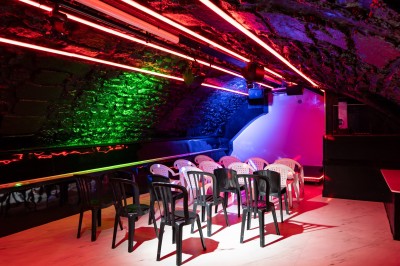 Salle voûtée en pierre avec éclairage LED coloré, mobilier minimaliste et comptoir de bar au fond.