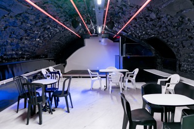 Salle voûtée en pierre avec éclairage LED coloré, mobilier minimaliste et comptoir de bar au fond.