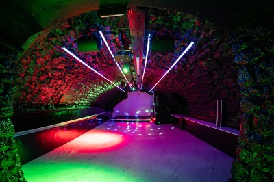 Salle voûtée en pierre avec éclairage LED coloré, mobilier minimaliste et comptoir de bar au fond.