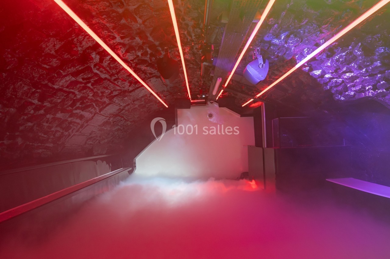 Salle voûtée avec éclairage rouge et violet, sol couvert de fumée artificielle.