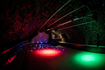 Salle voûtée en pierre avec éclairage LED coloré, mobilier minimaliste et comptoir de bar au fond.