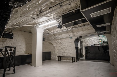 Salle voûtée en pierre avec éclairage LED coloré, mobilier minimaliste et comptoir de bar au fond.