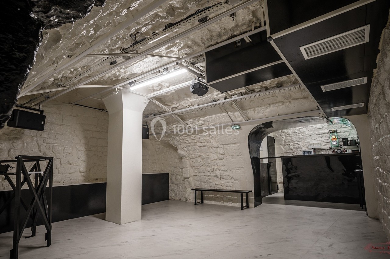 Salle voûtée en pierre blanche avec éclairage moderne, mobilier minimaliste et comptoir au fond.