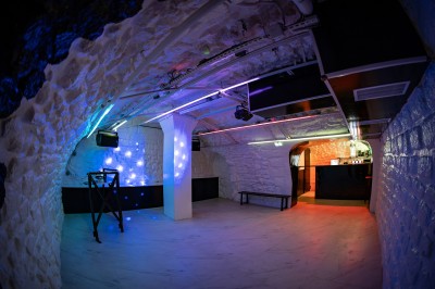 Salle voûtée en pierre avec éclairage LED coloré, mobilier minimaliste et comptoir de bar au fond.