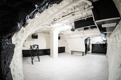 Salle voûtée en pierre avec éclairage LED coloré, mobilier minimaliste et comptoir de bar au fond.