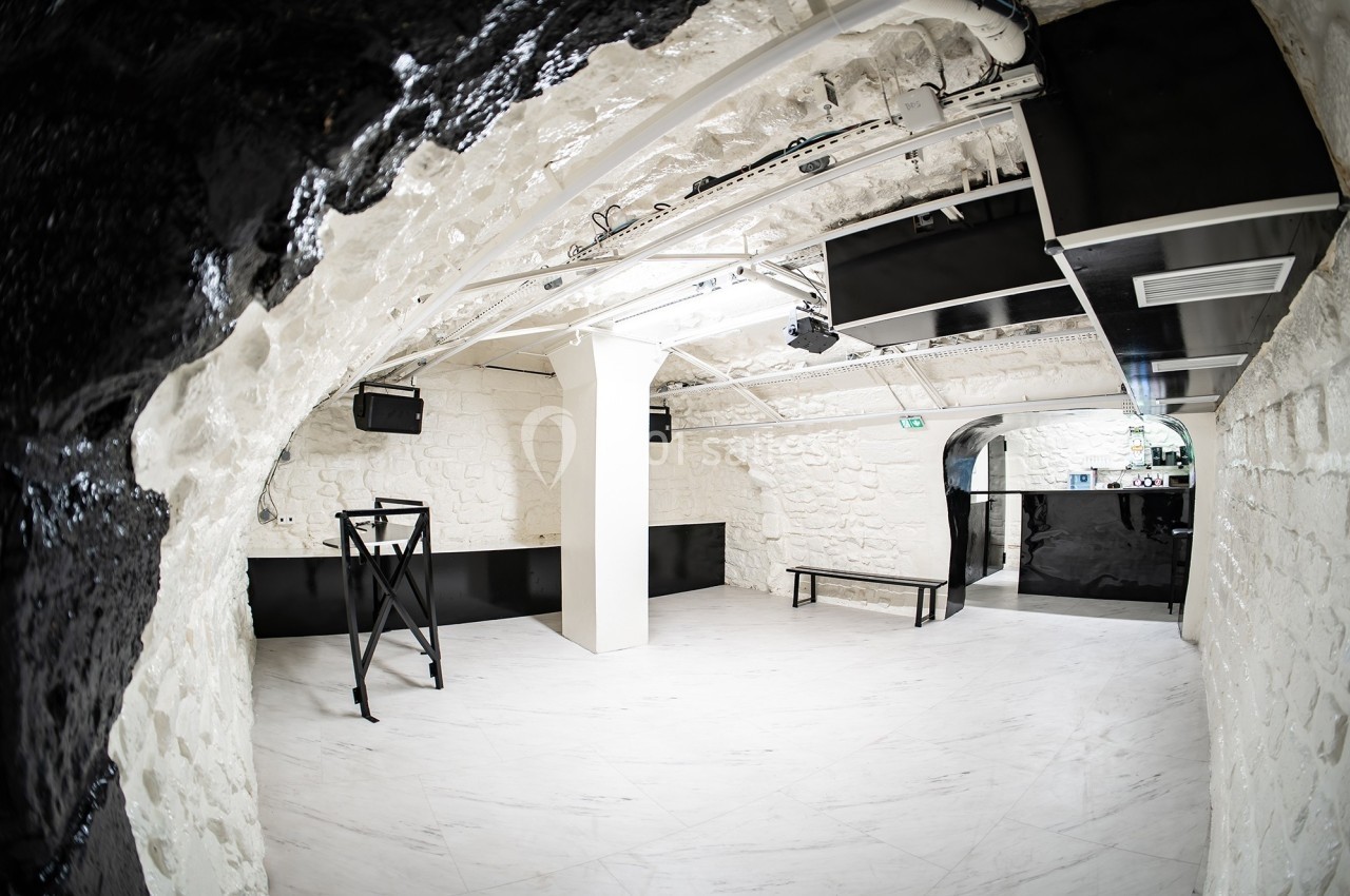 Salle voûtée avec murs en pierre blanche, sol en marbre clair, mobilier noir minimaliste et éclairage moderne.