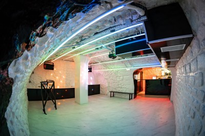 Salle voûtée en pierre avec éclairage LED coloré, mobilier minimaliste et comptoir de bar au fond.