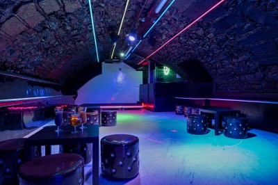 Miniature Location salle Paris 1 (Paris) - Merry #11 Bar avec comptoir noir, éclairé par des néons rouges et verts, dans une pièce aux murs en pierre apparente.