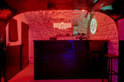 Miniature Location salle Paris 1 (Paris) - Merry #18 Bar avec comptoir noir, éclairé par des néons rouges et verts, dans une pièce aux murs en pierre apparente.