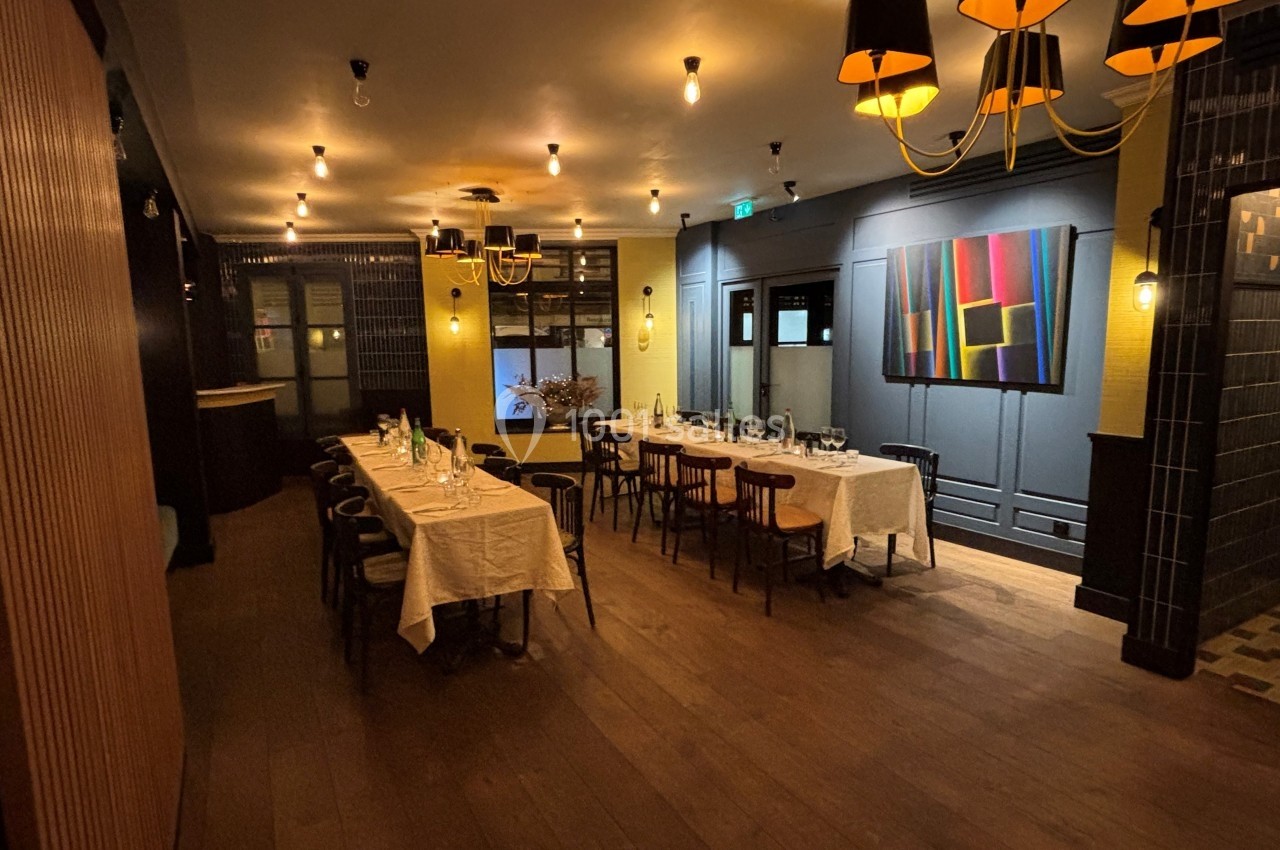 Salle de restaurant élégante avec longues tables dressées, éclairage chaleureux et décoration moderne.