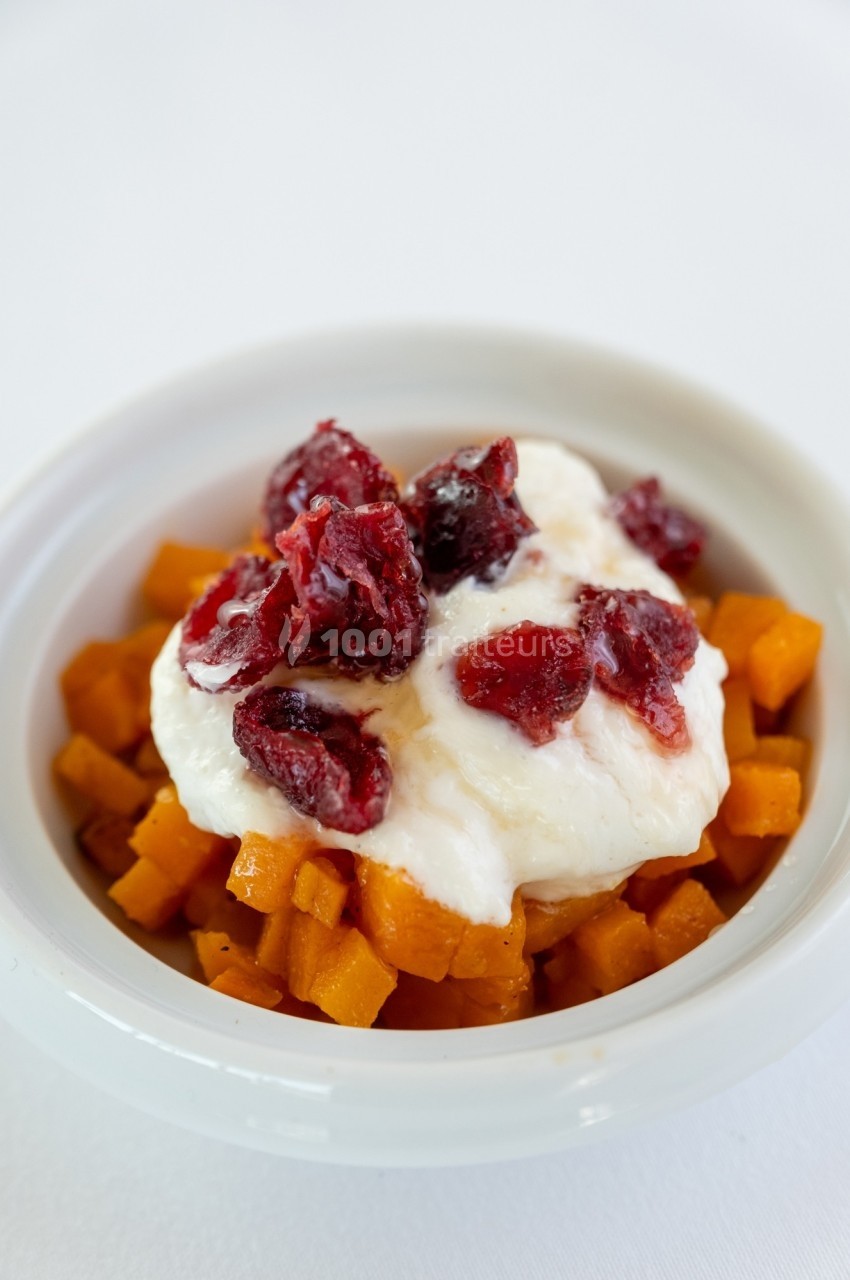 Bol contenant des dés de patate douce, garnis de yaourt et de morceaux de canneberges.