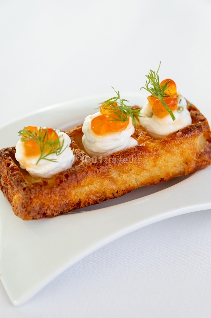 Gaufre dorée garnie de crème, œufs de poisson et brins d'aneth, servie sur une assiette blanche.