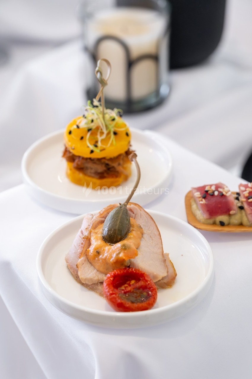 Assiette de bouchées raffinées comprenant viande, légumes et garnitures, présentées sur une nappe blanche.
