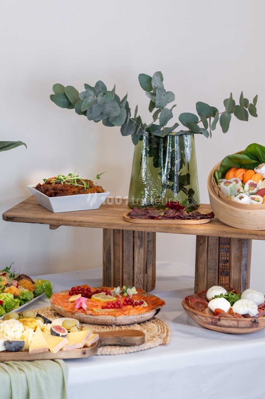 Buffet avec plats variés, incluant tarte, salade, fromage, charcuterie et un vase décoratif avec des branches d'eucalyptus.