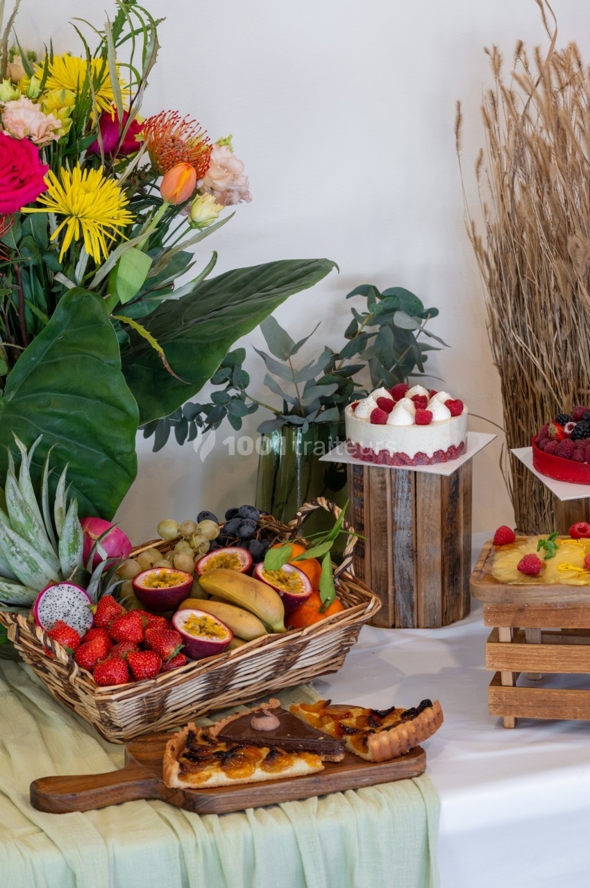 Plateau de fruits tropicaux, tarte aux fruits, gâteau à la crème et fleurs décoratives sur une table.