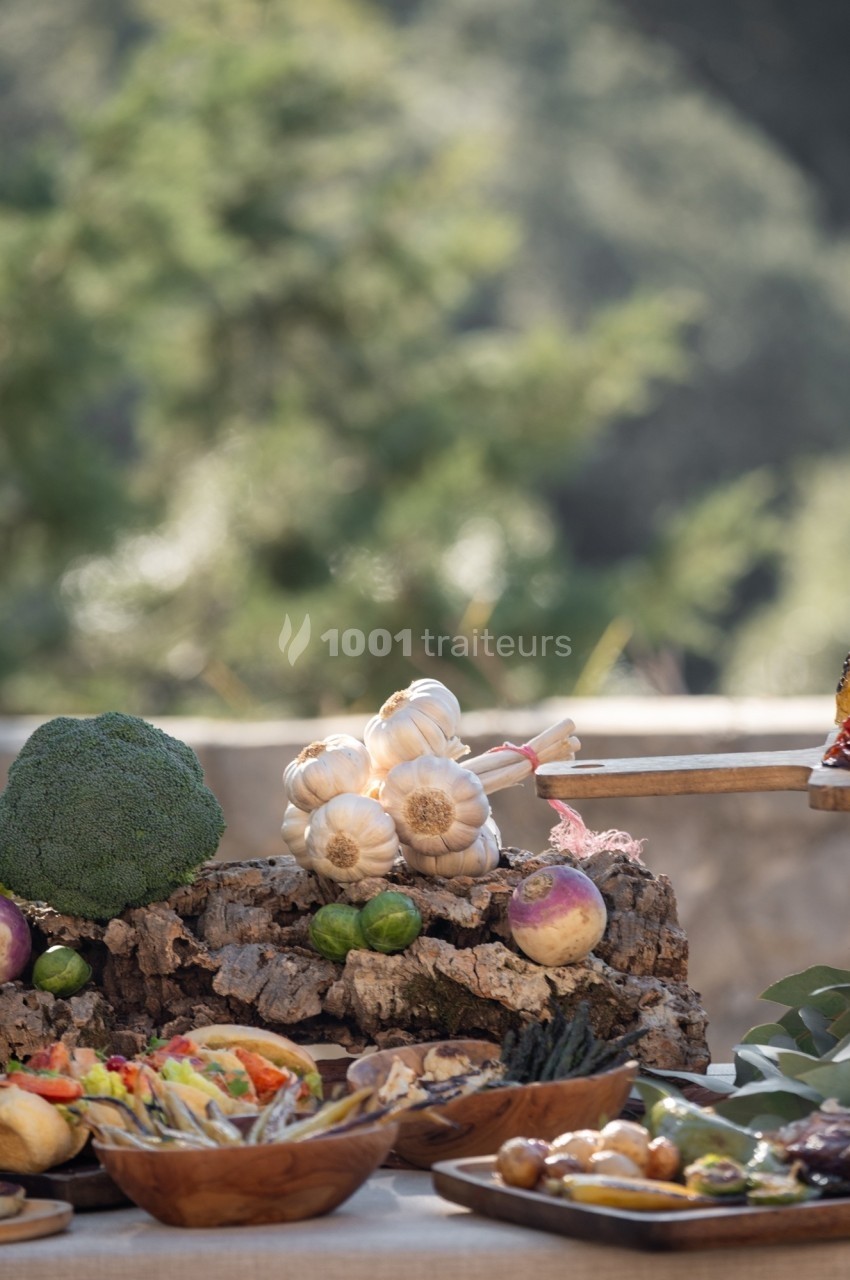 Des légumes frais, dont de l'ail, du brocoli et des navets, disposés sur une table en extérieur avec un fond naturel.