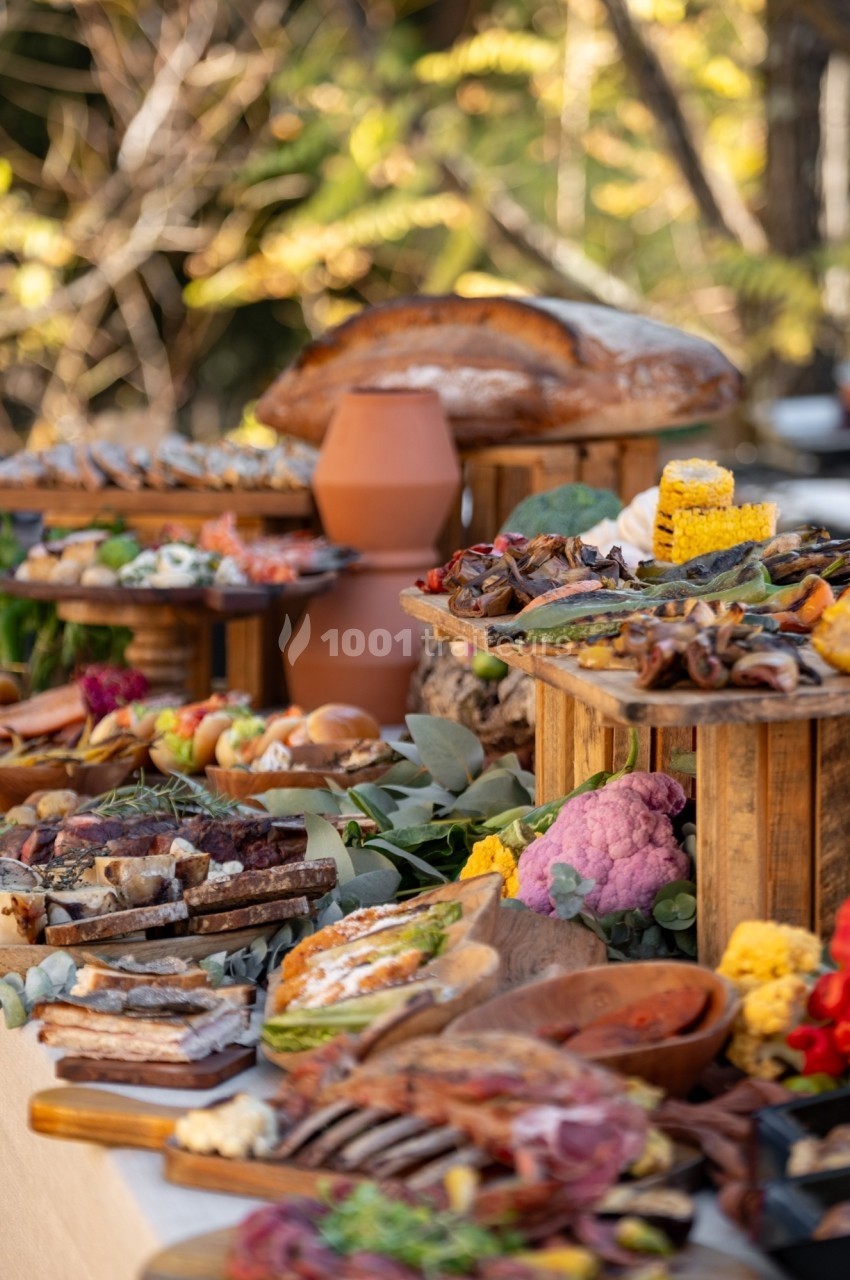 Buffet en plein air avec divers plats, pains, légumes colorés et charcuteries disposés sur des plateaux en bois.