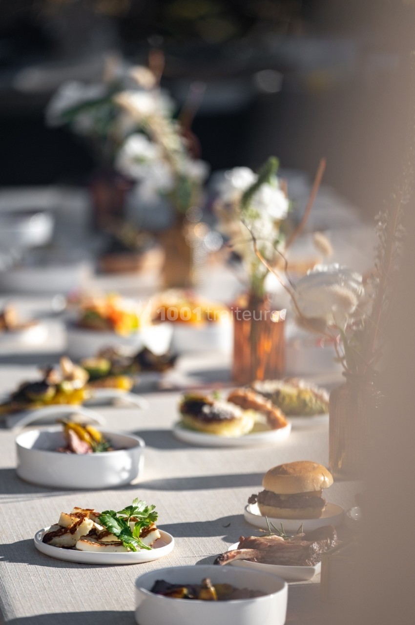 Table dressée en extérieur avec divers plats et décorations florales dans une lumière douce.