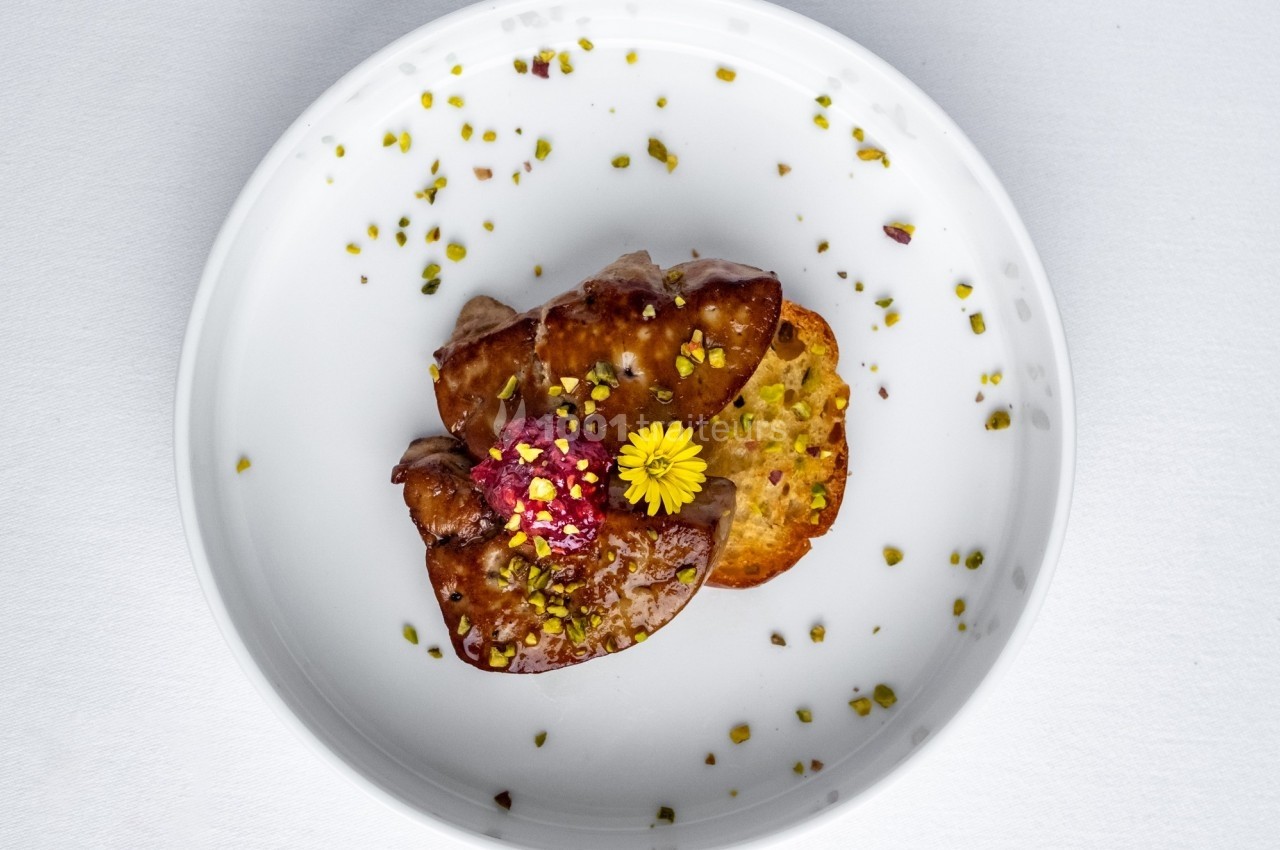 Assiette contenant une tranche de foie gras, une garniture florale, des éclats de pistache et une tranche de pain.