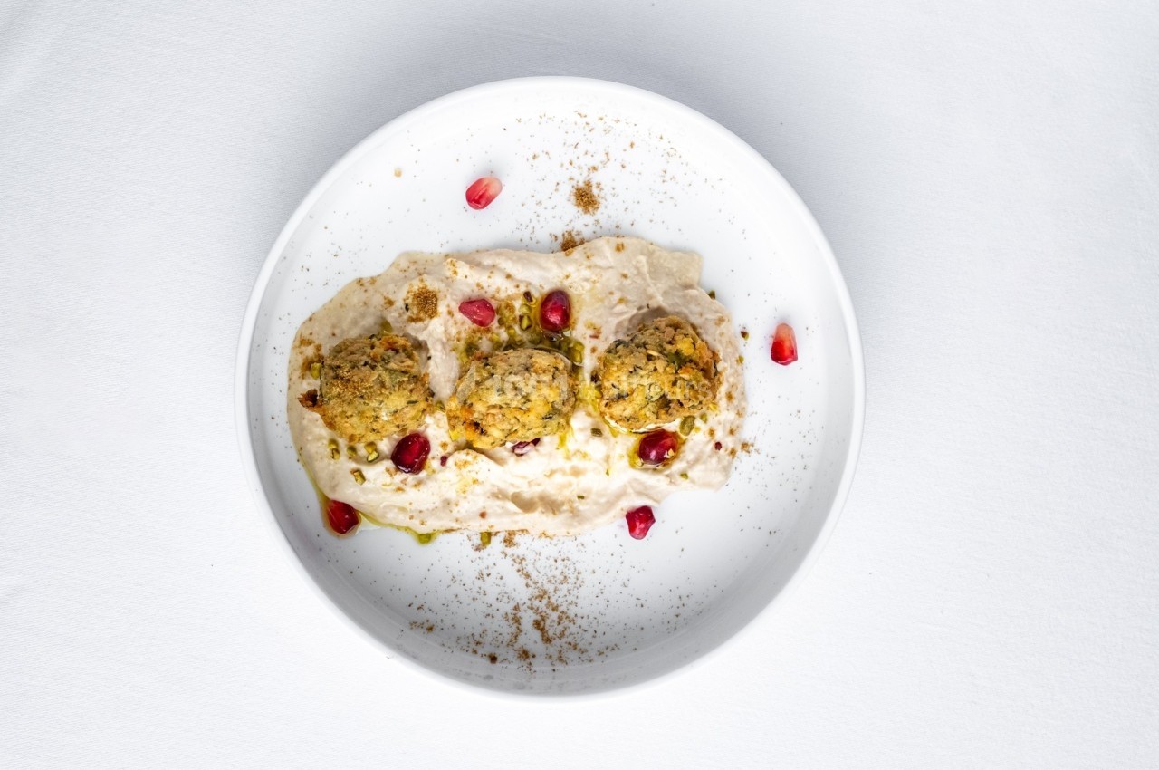 Assiette contenant trois falafels sur un lit de houmous, garnis de graines de grenade et d'épices.