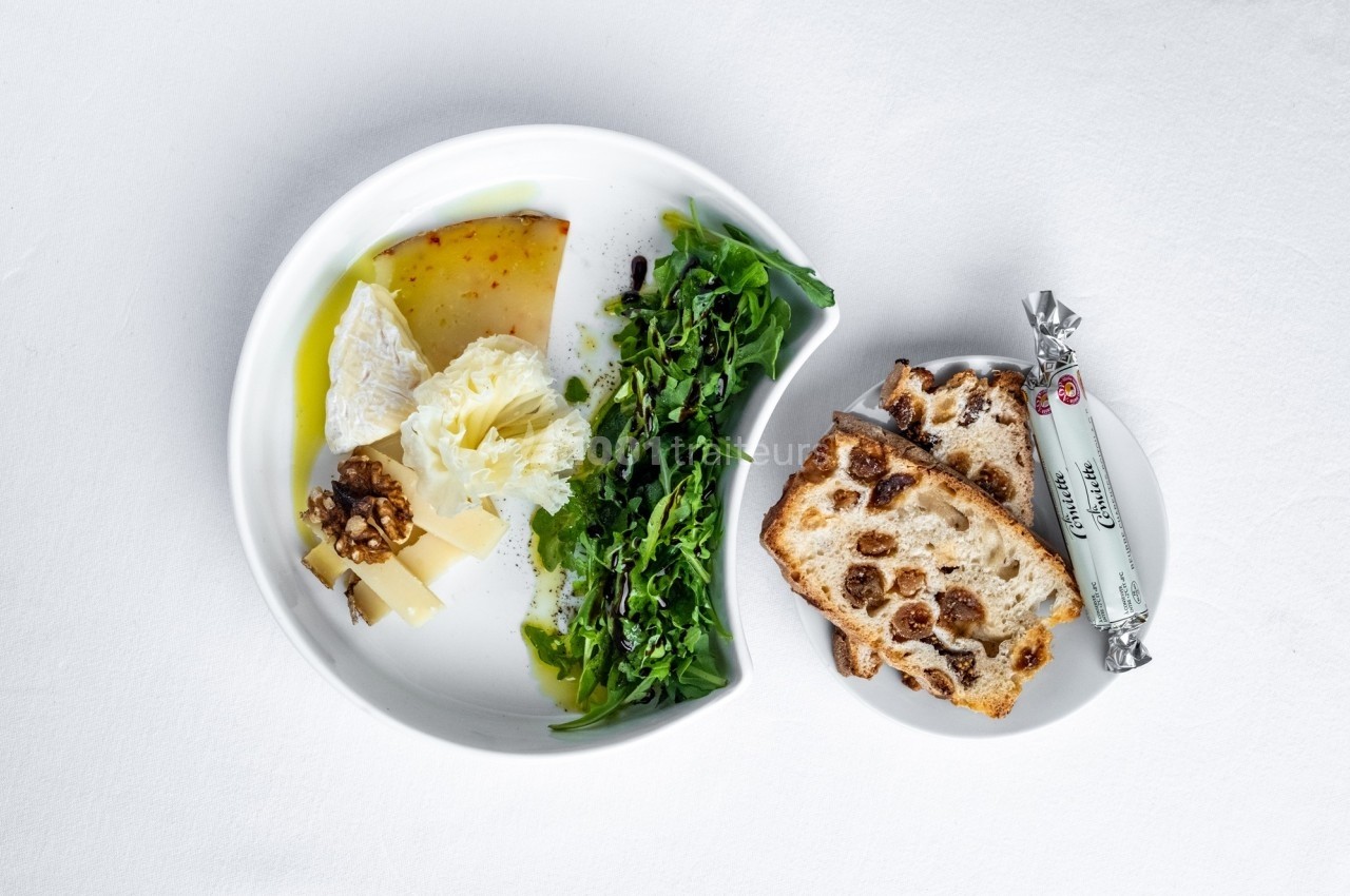 Assiette avec fromages variés, noix, roquette, huile d'olive et tranches de pain aux fruits secs.