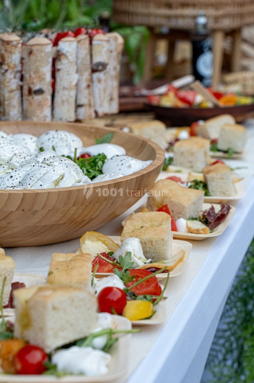 Buffet avec salade de mozzarella, légumes frais, focaccia et divers plats disposés sur une table blanche.