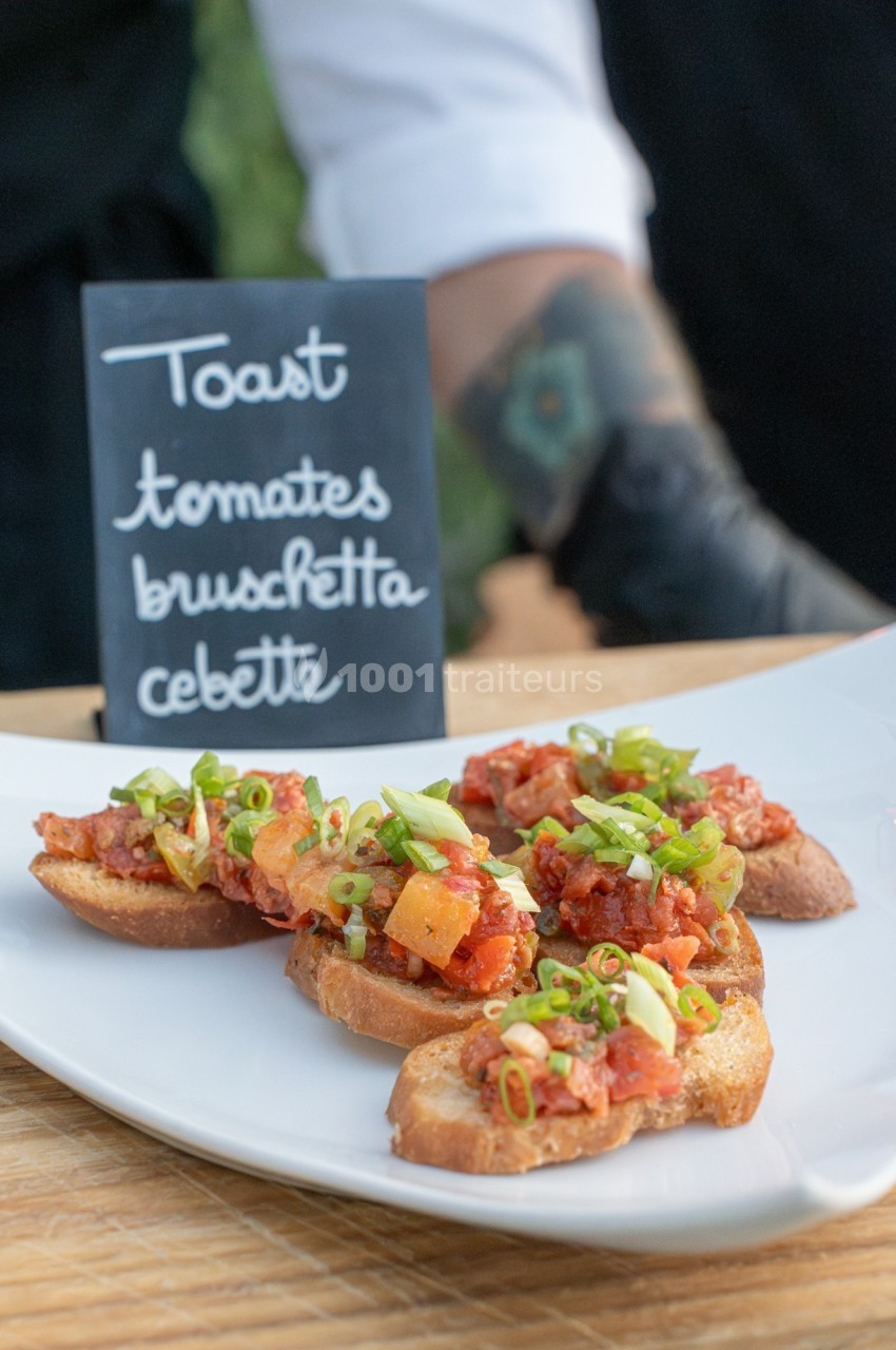 Toasts garnis de tomates, cébette et herbes fraîches, présentés sur une assiette blanche avec une ardoise descriptive.