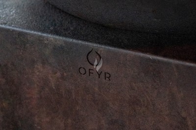 Logo ’OFYR’ gravé sur une surface métallique sombre et texturée.