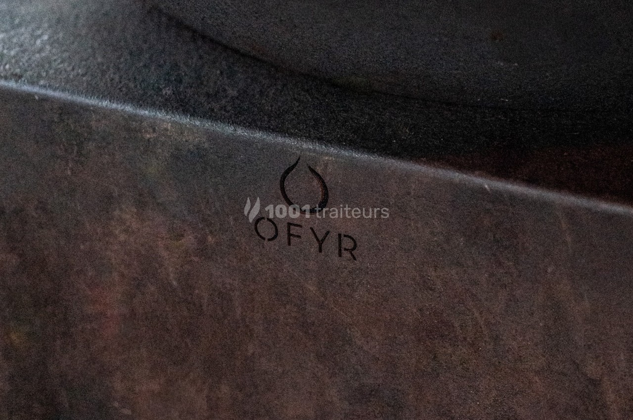 Logo ’OFYR’ gravé sur une surface métallique sombre et texturée.