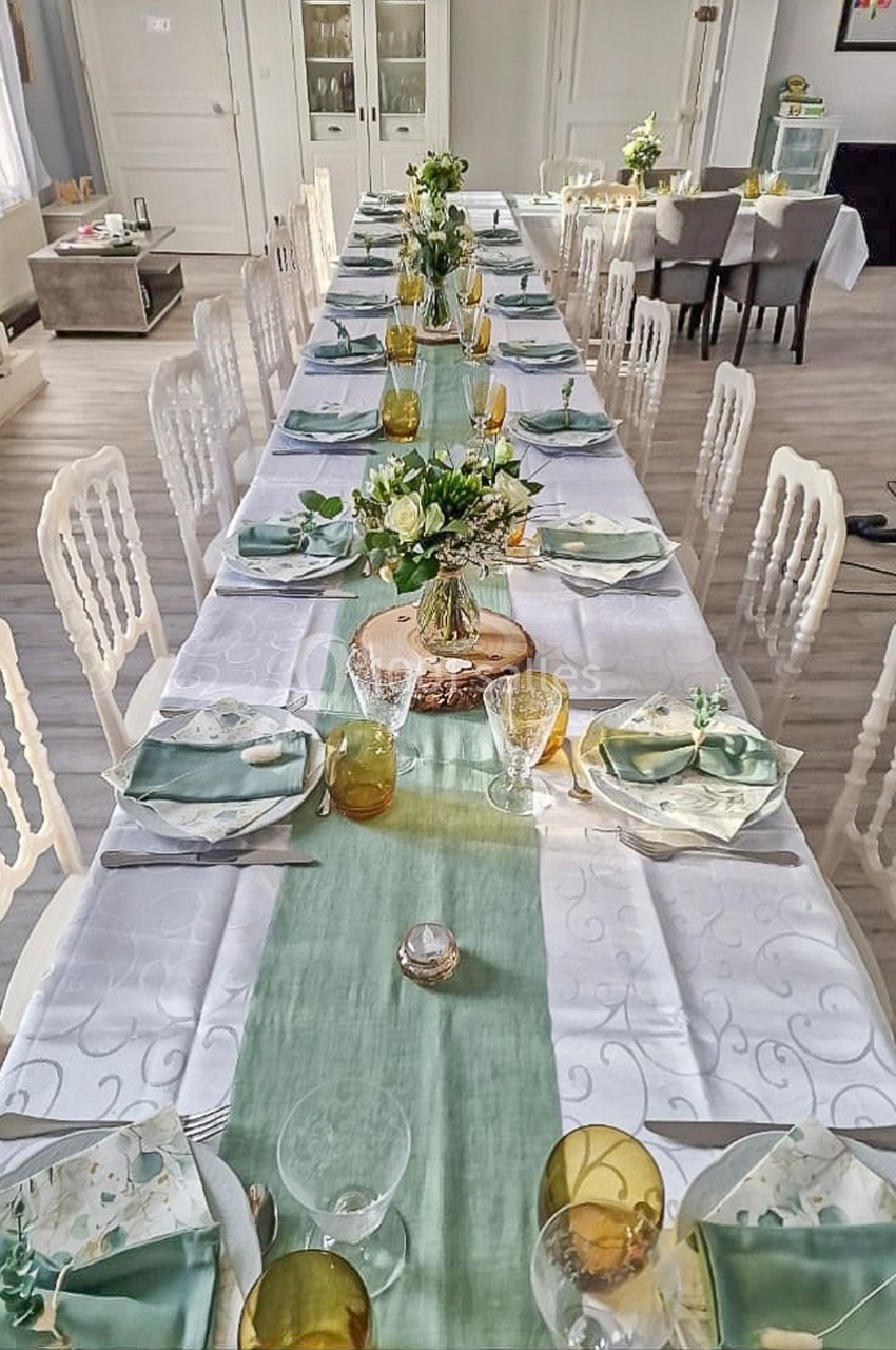 Table dressée pour un repas, décorée avec une nappe blanche, un chemin de table vert et des bouquets de fleurs.