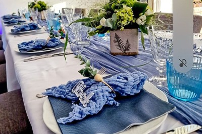 Table dressée avec une assiette blanche, une serviette rose ornée d'une feuille argentée, et des couverts cuivrés.