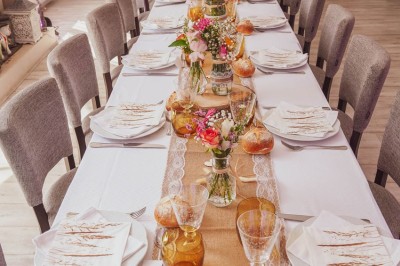 Table dressée avec une assiette blanche, une serviette rose ornée d'une feuille argentée, et des couverts cuivrés.