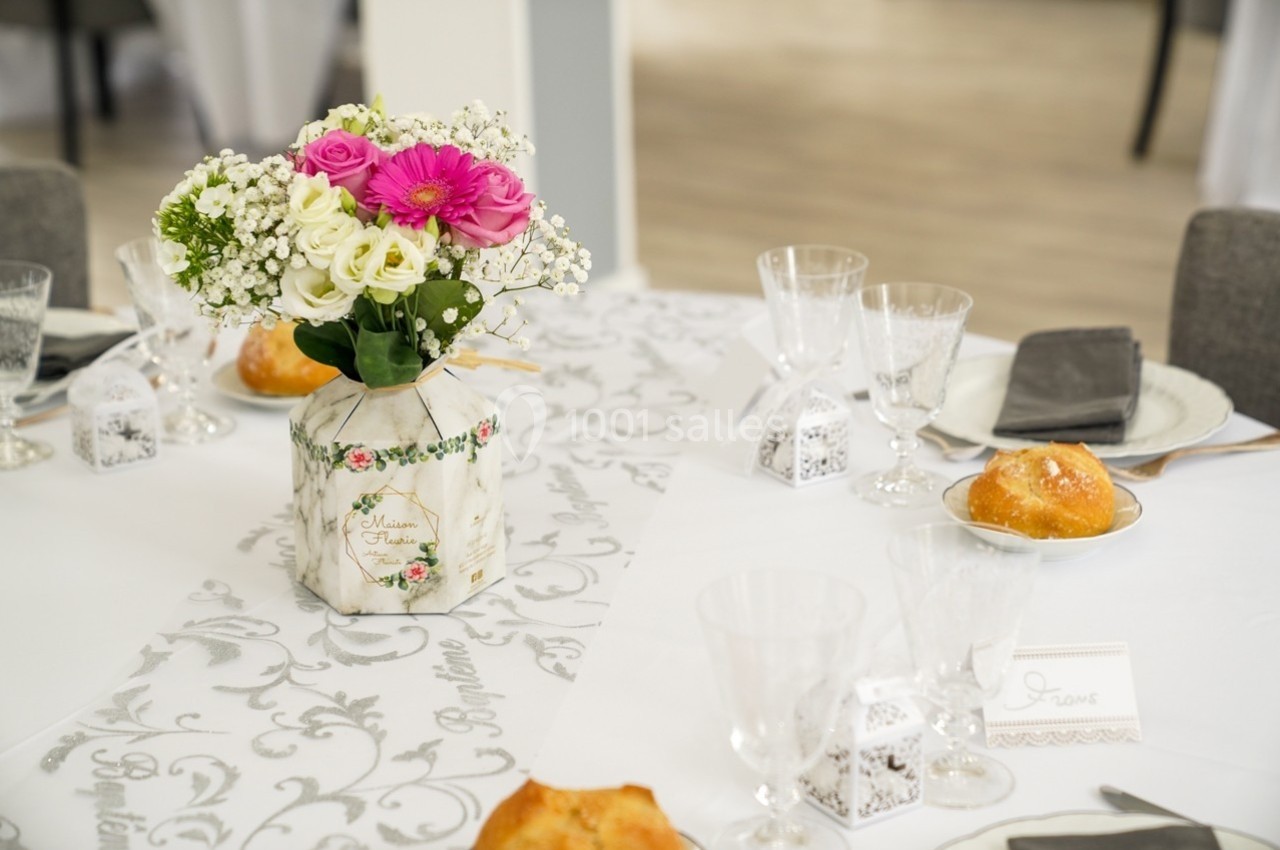 Centre de table avec bouquet de fleurs roses et blanches, entouré de vaisselle et de décorations de mariage.