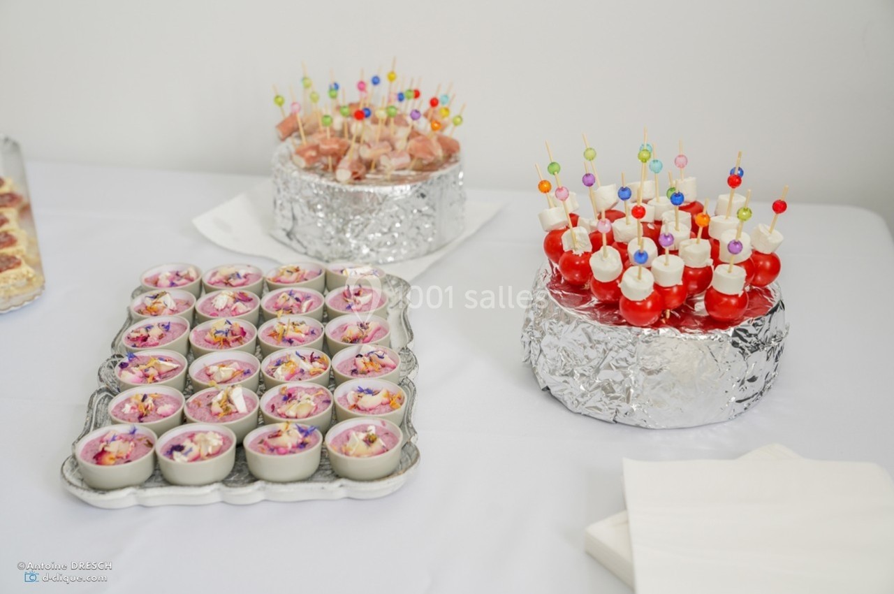 Plateau de verrines colorées et assortiments de brochettes apéritives disposés sur une table blanche.