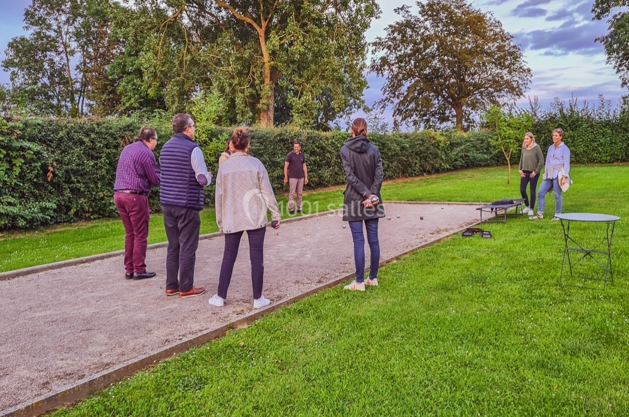 Des personnes jouent à la pétanque sur un terrain extérieur entouré de verdure et d'arbres.