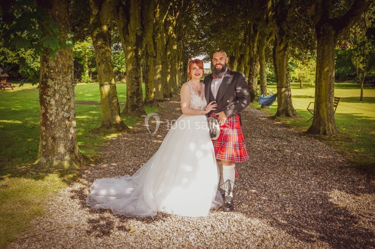 Un couple en tenue de mariage pose sur un chemin bordé d'arbres dans un cadre verdoyant.