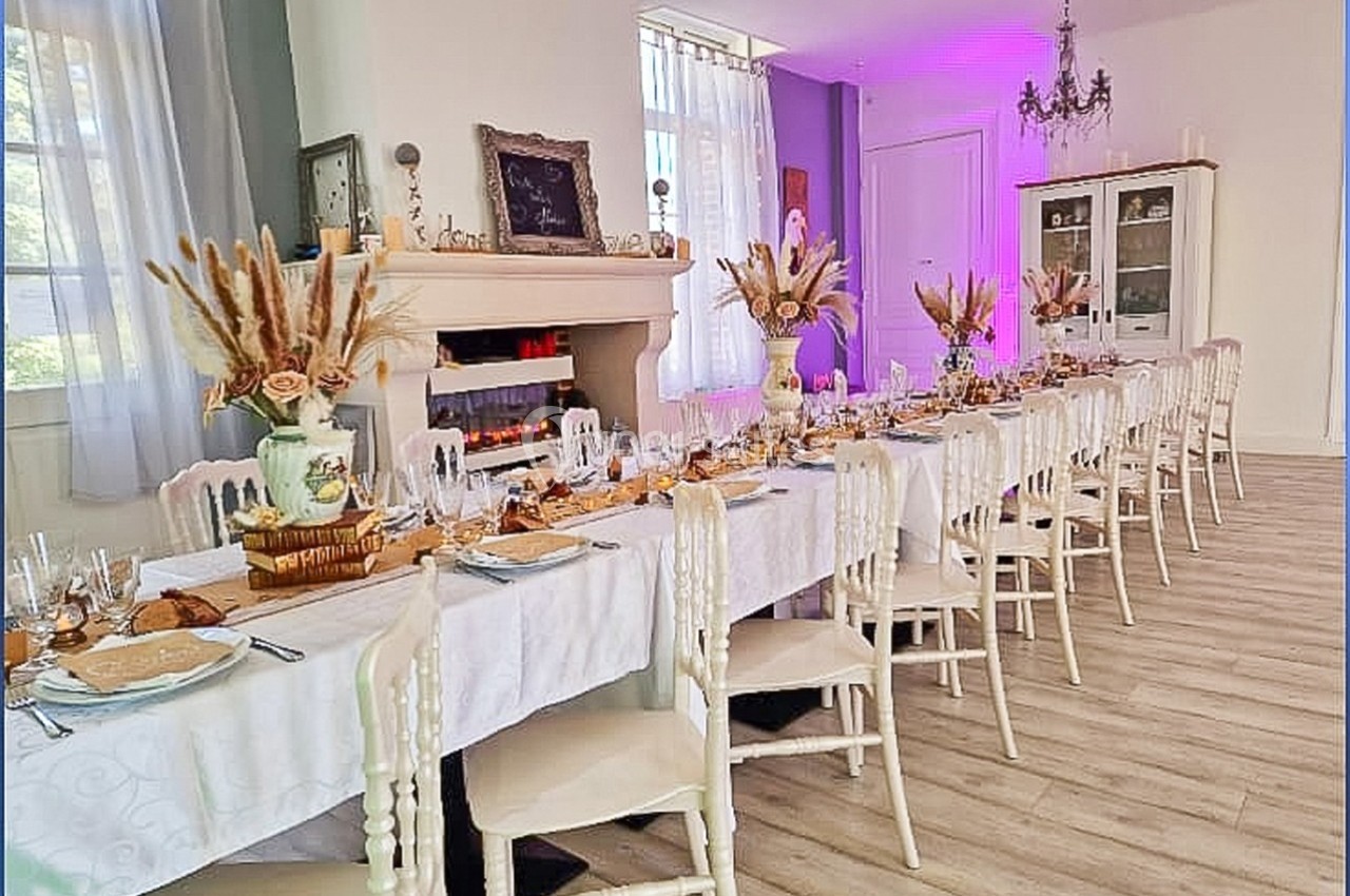 Table longue élégamment dressée avec nappes blanches, décorations florales et ambiance lumineuse violette en arrière-plan.