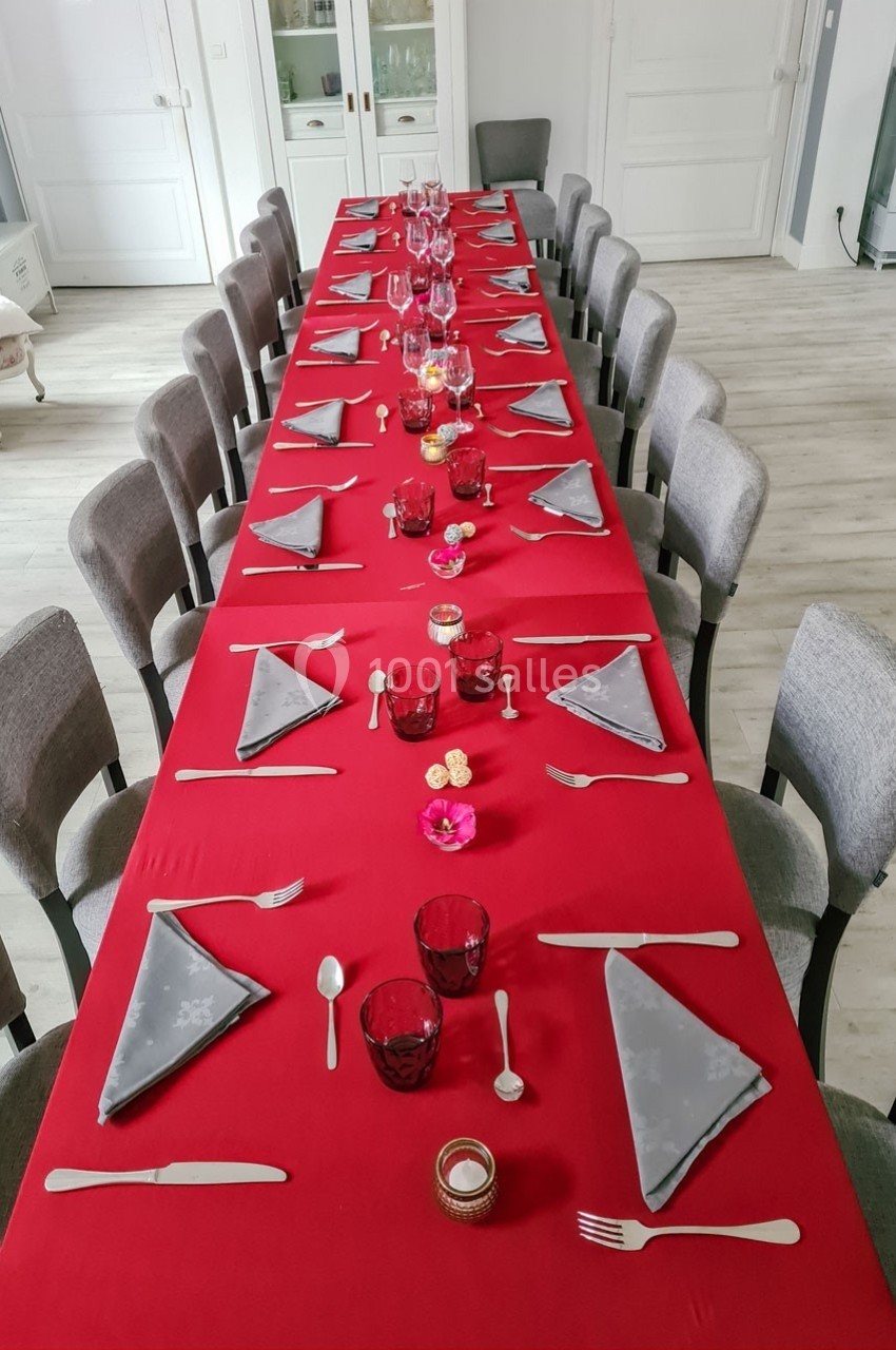 Table dressée avec une nappe rouge, des serviettes grises pliées, des verres rouges et des couverts alignés.