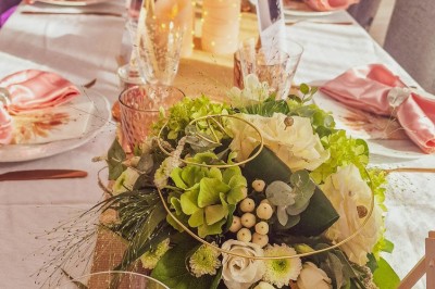 Table dressée avec une assiette blanche, une serviette rose ornée d'une feuille argentée, et des couverts cuivrés.