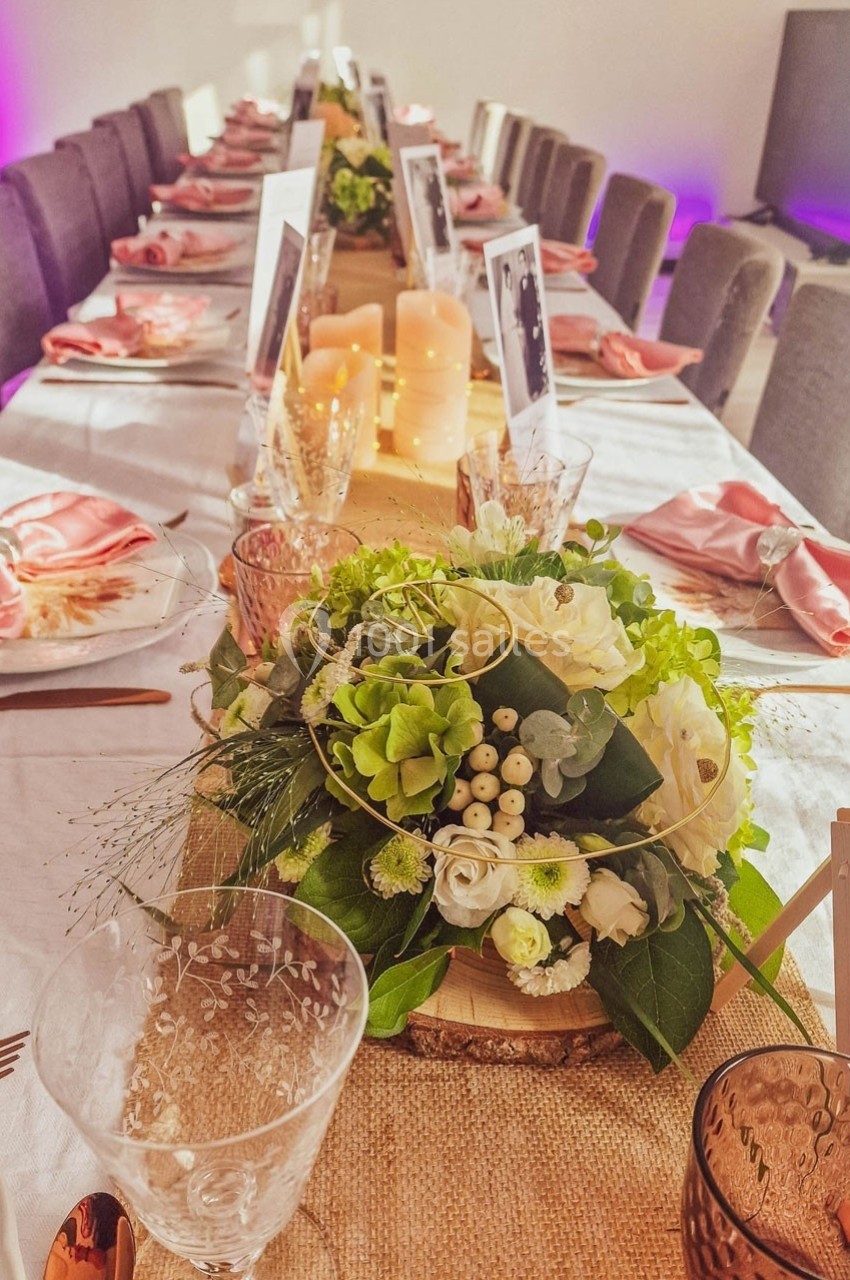 Table décorée pour un événement avec nappes blanches, serviettes roses, bougies et centre de table floral.