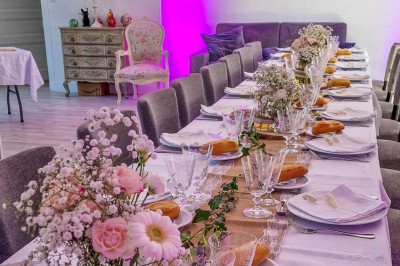 Table dressée avec une assiette blanche, une serviette rose ornée d'une feuille argentée, et des couverts cuivrés.