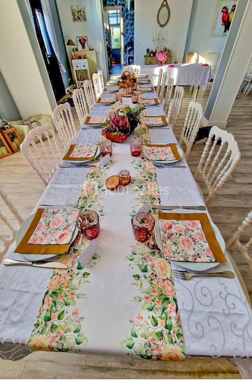 Table dressée avec une nappe blanche, un chemin de table fleuri, des assiettes décorées et des verres roses.