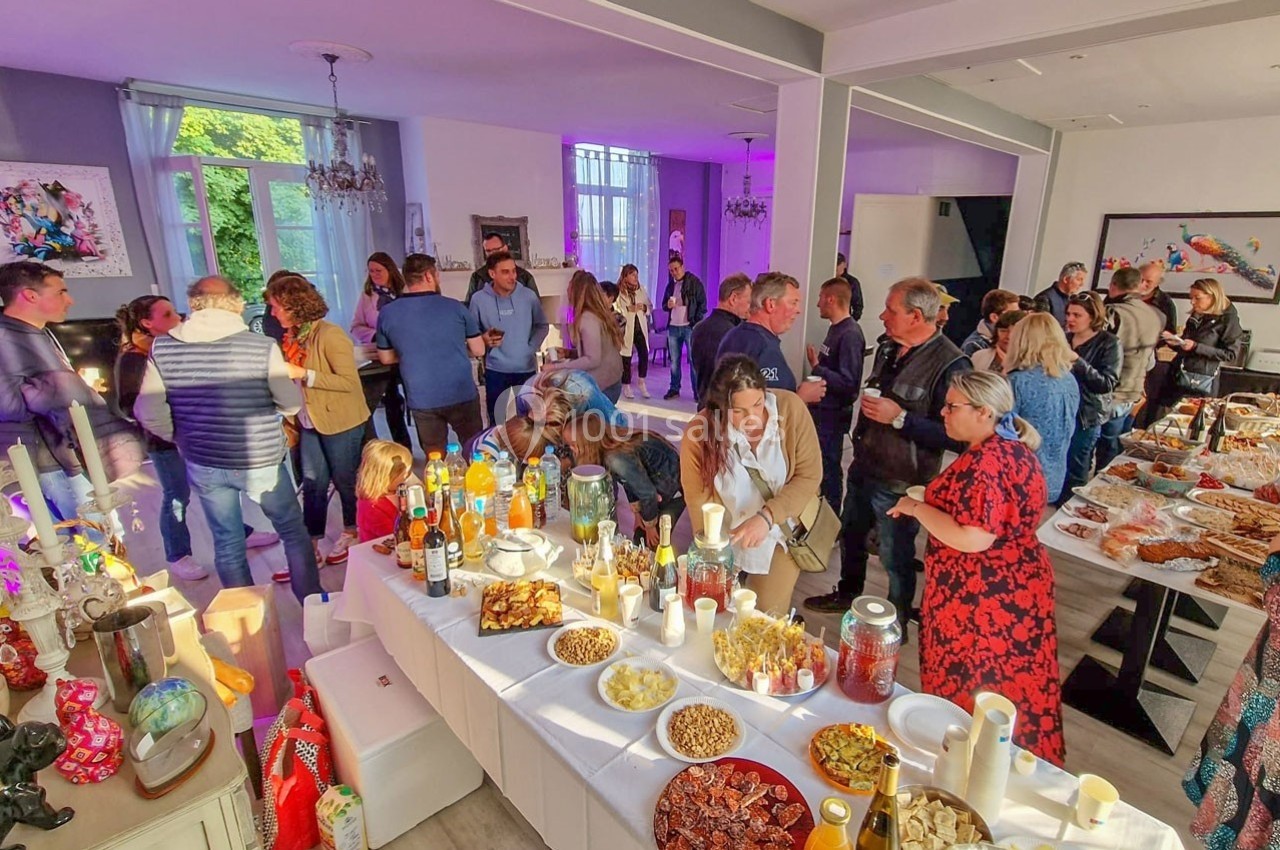 Groupe de personnes réunies dans une salle lumineuse autour de tables garnies de plats et boissons variés.
